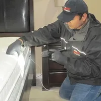 Bed bug inspection technician checking a mattress and bed frame for signs of infestation in Lowell, MA