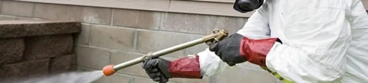 Pest control technician applying exterior insect treatment along a home foundation in Lowell, MA