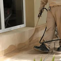 General pest control technician spraying exterior perimeter around a home in Lowell, MA