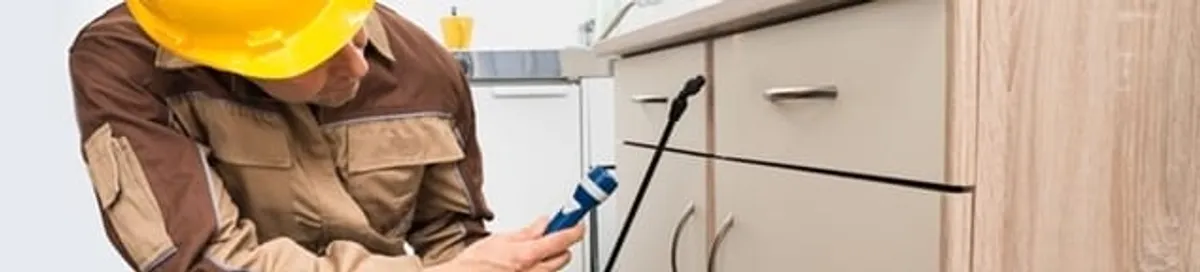Roach exterminator applying treatment under kitchen cabinets in Lowell, MA