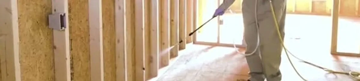 Termite treatment technician applying spray along framing and unfinished walls in Lowell, MA