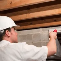 Termite inspection technician checking a basement wall and framing for termite activity in Lowell, MA
